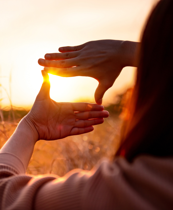 Chica de espaldas mostrando el sol con sus manos